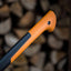 Manico di ascia ergonomico arancione e nero, primo piano, con sfondo di tronchi di legno sfocati. Strumento ideale per taglio di legna e lavori di giardinaggio. Design resistente e confortevole per un uso prolungato.